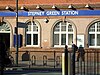 A red-bricked building with a rectangular, dark blue sign reading "STEPNEY GREEN STATION" in white letters and a man walking in front