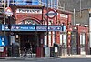 A red-bricked building with a rectangular, white sign reading "ENTRANCE" in black letters and a rectangular, blue sign reading "MAIDA VALE STATION"