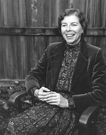 Portrait of woman with short, wavy hair, wearing an oversized velvet blazer over a floral dress