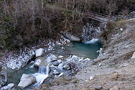 Rivière bordée par des rochers passant sous un pont en bois.