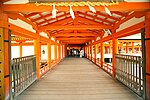 Roofed wooden corridor over water with red beams.