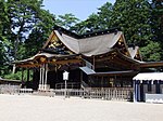 Wooden building with a large roof and central gable on the front. Both the roof and the lower part are in very dark colors. Three ropes are hanging down from the front centre gable.