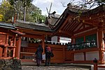 Building with white walls, red wooden beams and forked finials on the roof located behind a fence with gate.