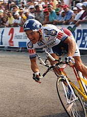 A cyclist on a bicycle, with spectators behind a fence.