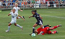 Marta vient d'éviter le gardien adverse, à terre. Deux adversaires se dirigent vers le but