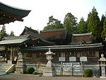 A complex of wooden buildings behind a wooden roofed fence.