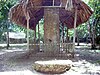 A hedged rectangular stone pillar with a leaf roof