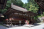 Three-quarter view of a proportionally tall wooden building with a veranda with red hand rail and a canopy covering the steps that lead to the central entrance. The roof appears to be a hip-and-gable roof.