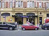 A gold-coloured building with a rectangular, dark blue sign reading "QUEENSWAY STATION" in white letters and people walking in front