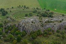 Photo d'un terrain comprenant un rempart bas et l'affleurement d'un rocher.