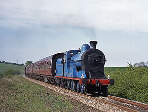 Great Northern Railway number 171 pulls a train of passenger coaches along a track through a field. The locomotive and tender are painted blue with gold lines, and red trim on her running boards; her smokebox and buffers are painted black. The coaches behind her are painted a reddish-brown, with black roofs.