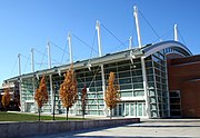 Ground-level view of a building with white poles sticking up from its sides and with trees in autumn colors in front of it