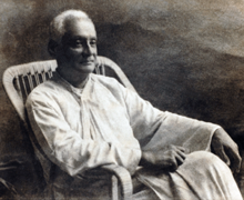 A black and white picture of a man sitting in a chair dressed in a white robe