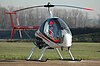 A white-nosed, red-tailed helicopter sits on the ramp, its red-tipped rotor blades trained fore and aft, grass stretching out to trees behind it