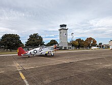 An airport control tower with a P-51 mustang plane sitting in front.