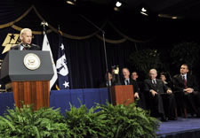 Biden speaking on podium with award winners seated behind. Click for larger image.