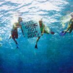 Realistic colored pencil drawing of four people underwater in scuba gear. Two in the middle hold sign reading 'It's getting hot down here!!'