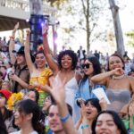 Row of students cheer with raised arms among crowd of graduation attendees