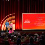 Jack Quaid and Zazie Beetz at podium next to large screen depicting the nominees for Animated Feature Film