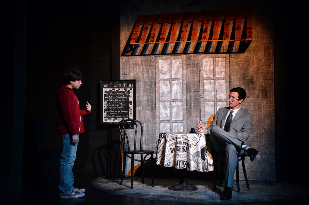 Man in a gray suit doing crossword puzzle outside a cafe looks at a young boy in a red hoodie.