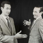 Paul Reubens and his character Pee-Wee Herman gesturing at a handshake