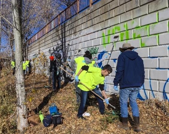 Photo of a group of people painting over graffiti on a wall outside.