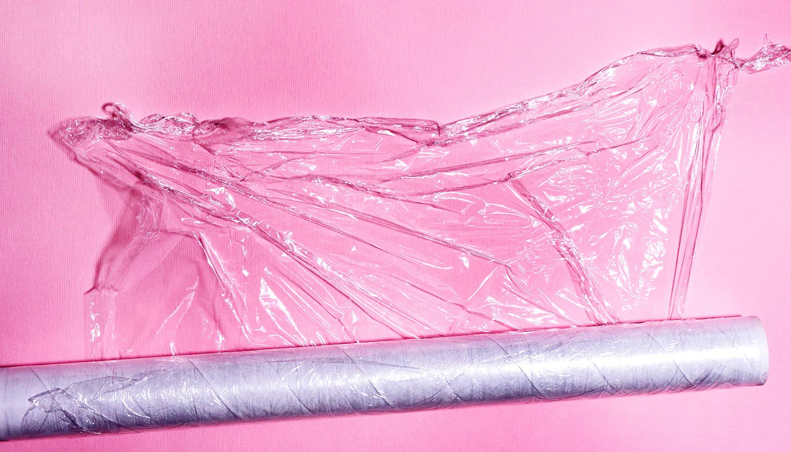 A roll of plastic wrap is unspooled on a pink surface.