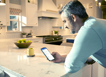 A man leaning on kitchen counter uses smartphone to compare payments and rates