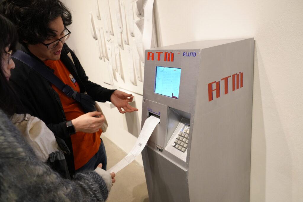 Two people standing next to an exhibition piece from the Data Through Design Aftermath exhibition - ATM Parcel.