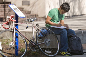 Person next to a bike writing in a notebook on steps at Boise State University