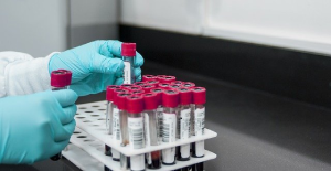 Photograph of several sample tubes in a white rack. A pair of blue-gloved hands is holding two of the samples.