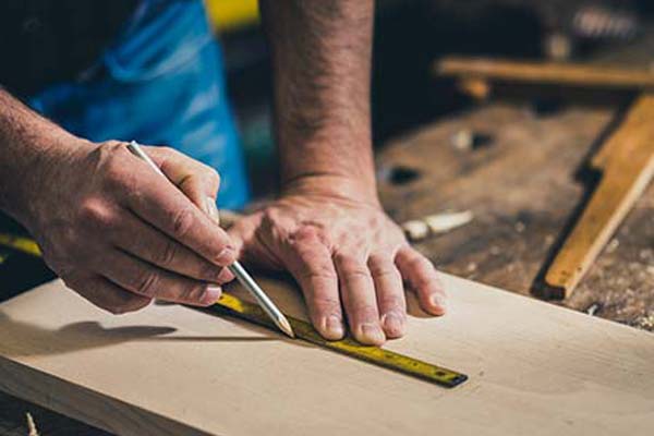 Close up image of a carpenter using a tape measure and wood pencil