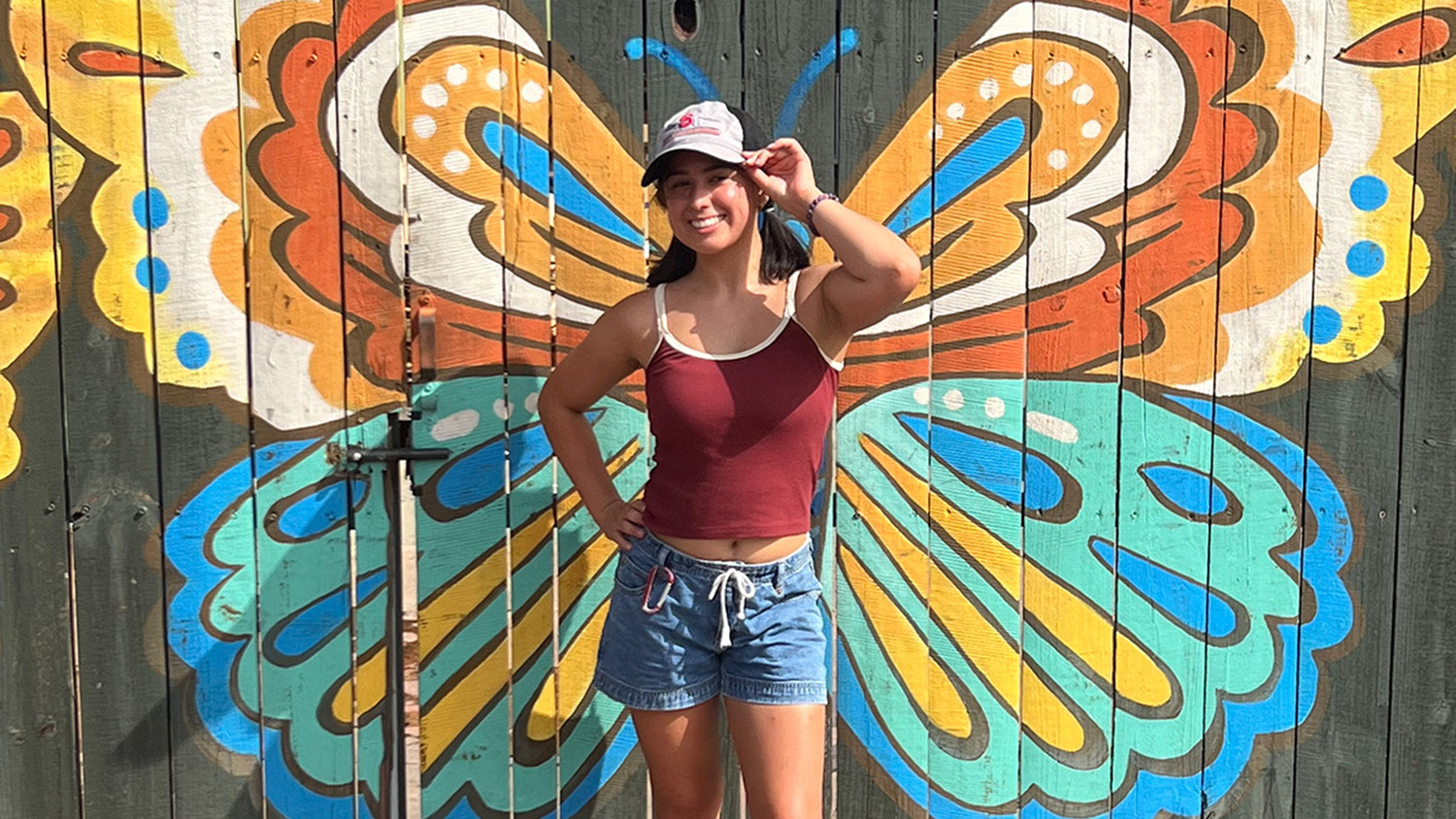 Young woman in red top and shorts in front of butterfly painting