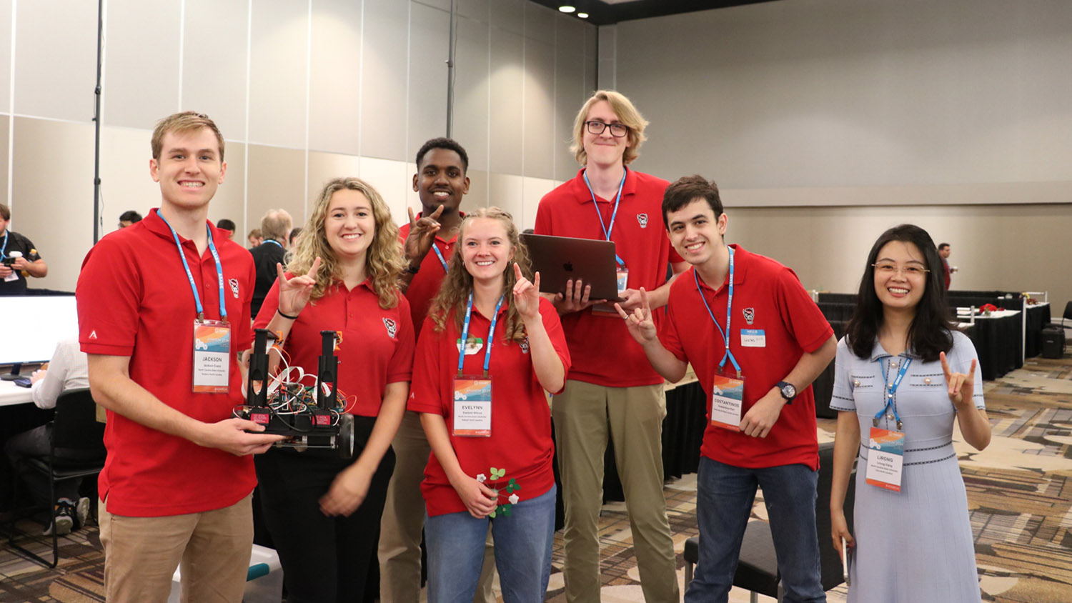 a group of people making wolf signs with their hands and holding a small robot