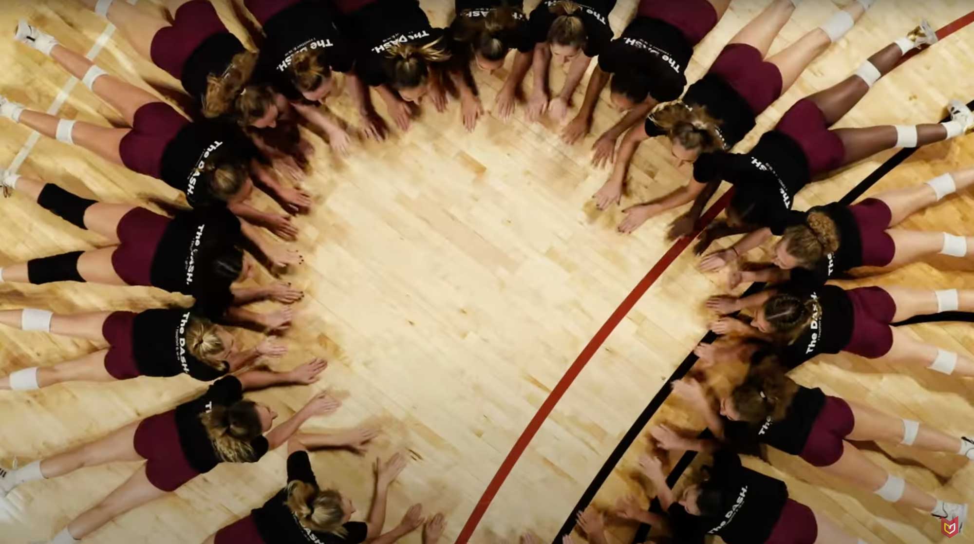 The Calvin women's volleyball team lay in a circle the gym floor, pounding the floor with their hands.