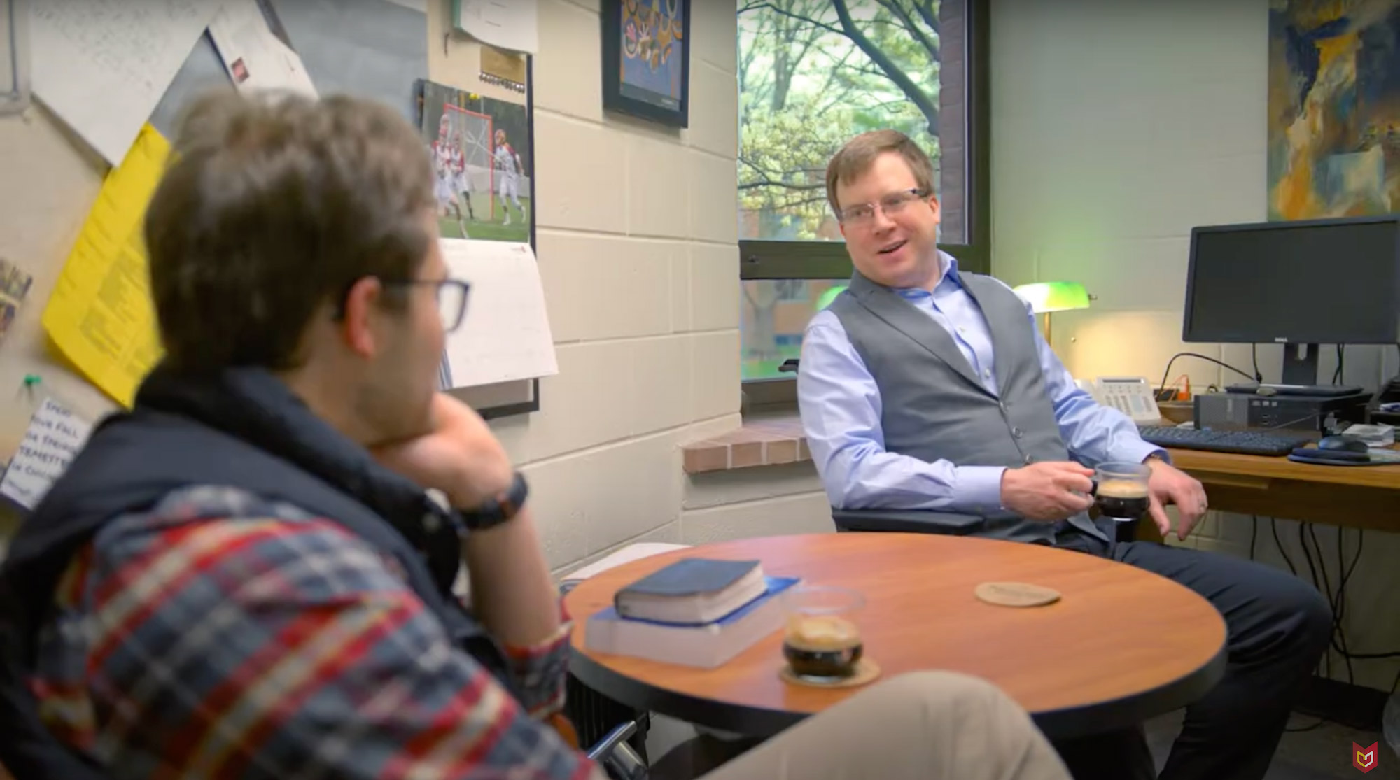 Professor Jason Stansbury sits in his office at a table, talking with a student.