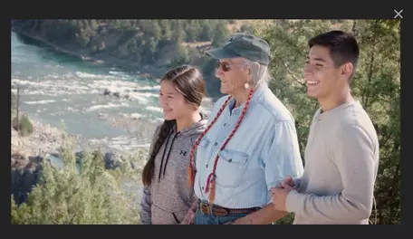 Videos Sreenshot, two children with an older woman smiling with a river and trees on the river bank behind them. 