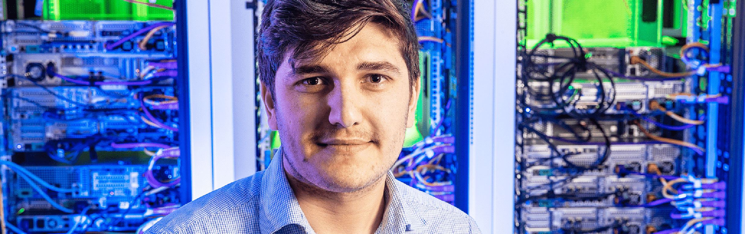 Computer science major standing in front of a rack of servers.