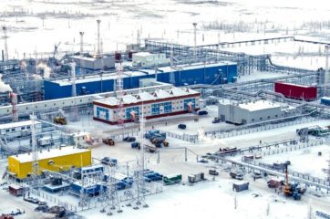 Industrial buildings on a snowy landscape with gas coming out of towers in the buildings.