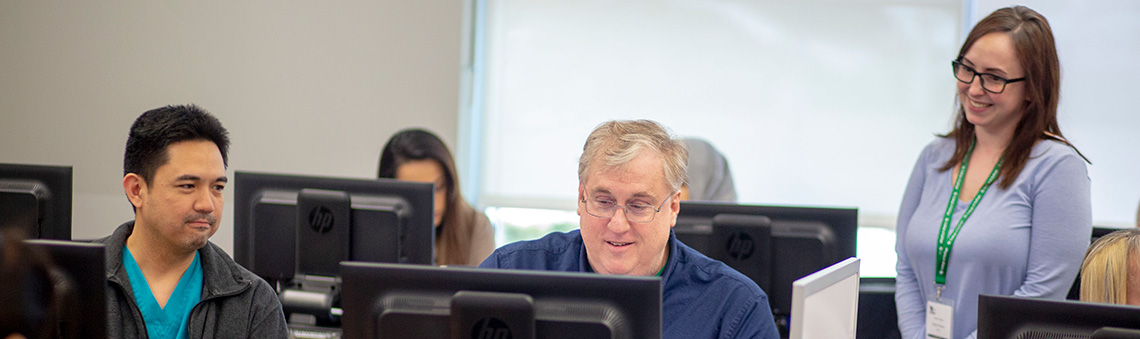 Woman helping students register for classes on computers in a computer lab