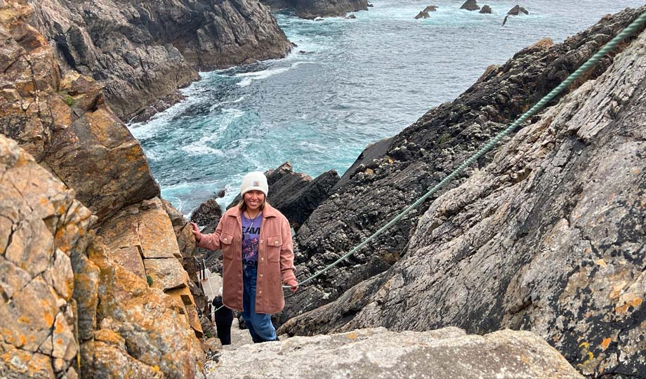 Lia Vanscoitt standing on a cliffside edge in Ireland with her hands up in the air