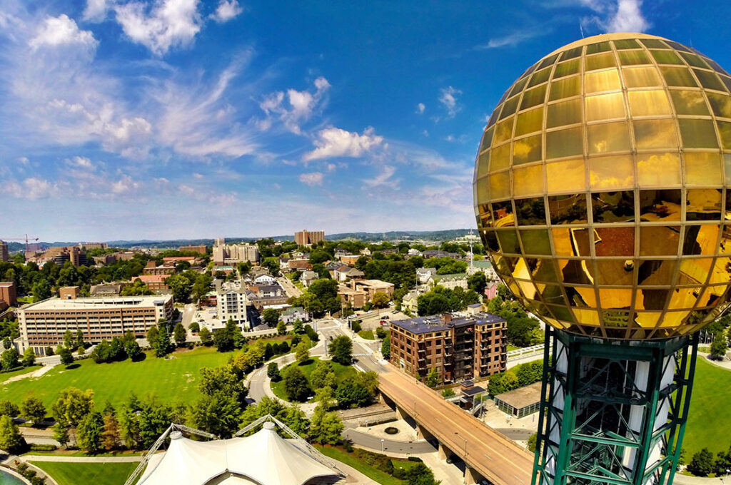 The gold globe of World's Fair Park glistens in the sunshine in front of an aerial view of Knoxville