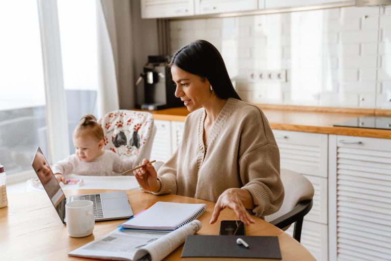 Young mother working with laptop, with her baby next to her.