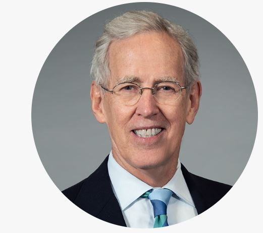 Bill, a older man with light skin tone, gray hair, and glasses, smiles in this professional headshot. He is wearing a black suit coat, white collared shirt and blue/green tie.