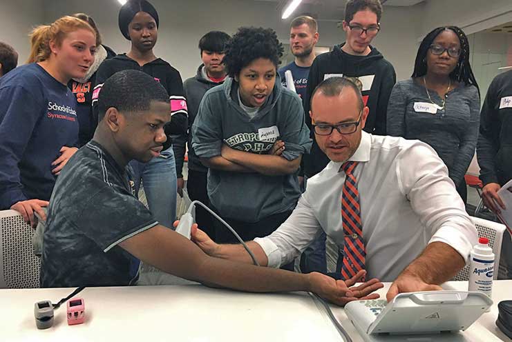 A group of students surround a professor using monitoring equipment