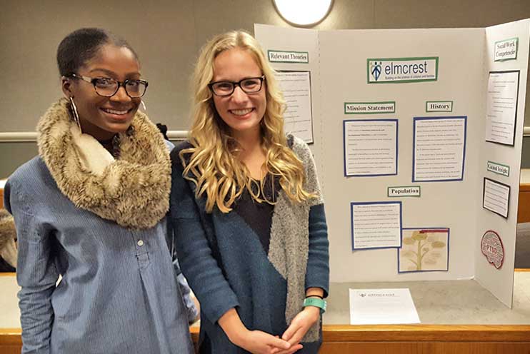 Two students stand besides a research poster