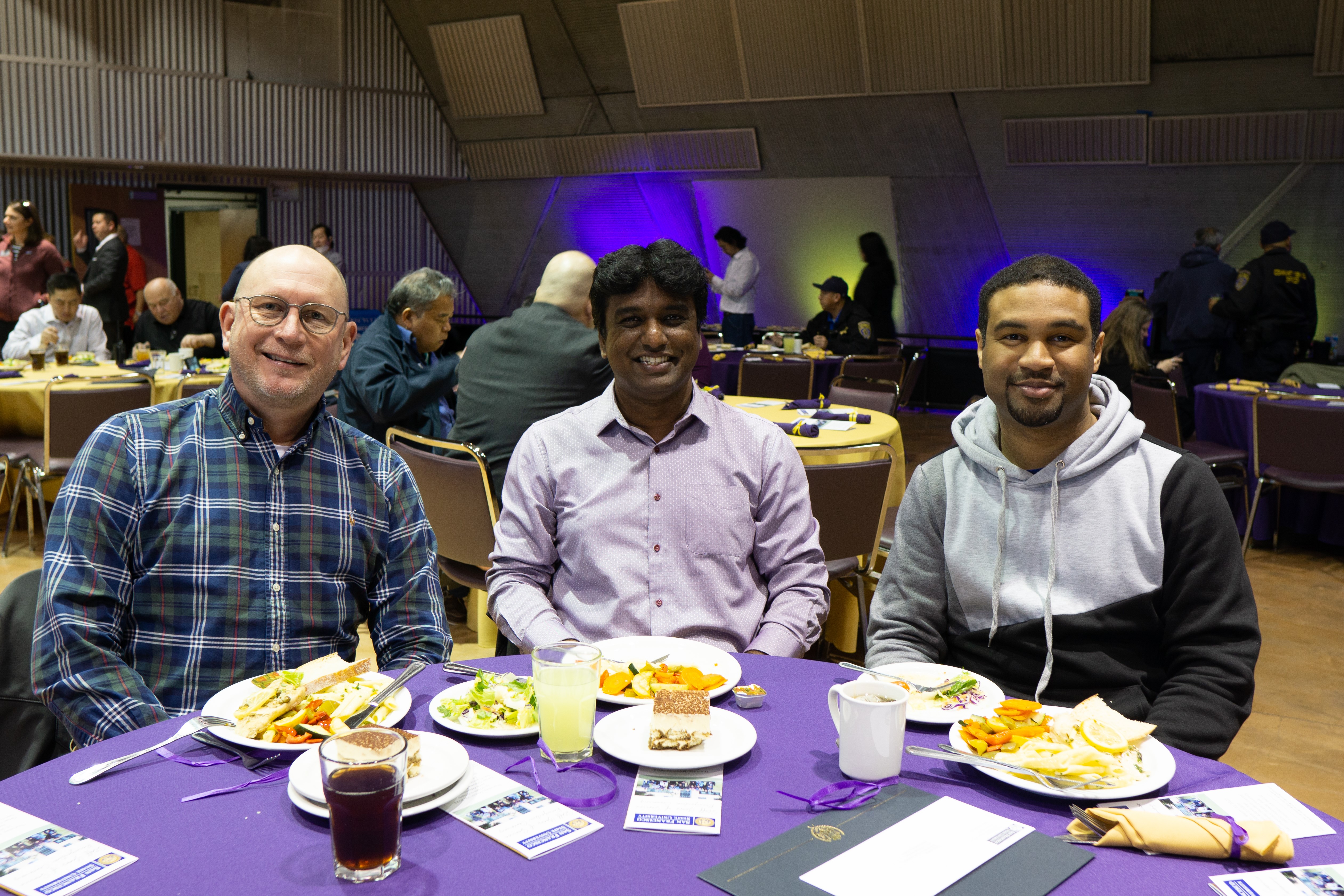 Three male employees eating lunch at a table smiling