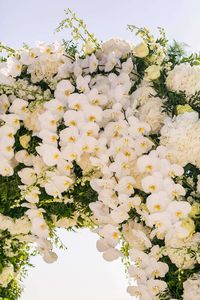 We set the scene with a sea of white orchids, lacing the couple’s ceremonial arch to match Carla’s wedding dress, festooning the terrace of their reception with round mirror surface tables, chandeliers and white bloom arrangements for days. Centerpiece magic brought by tree-branches vested with boules of candles and clear orchid and hydrangea filled vases was implemented with clear glass and gold rimmed dinnerware.