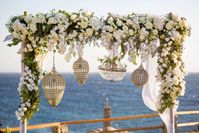 A luxury destination wedding  in Mykonos with white flowers and greenery. The gold details and the crystal chandeliers match perfectly with the beautiful scenery.