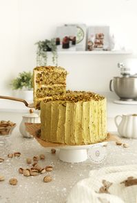 Pistachio cake on a white cake stand in a kitchen